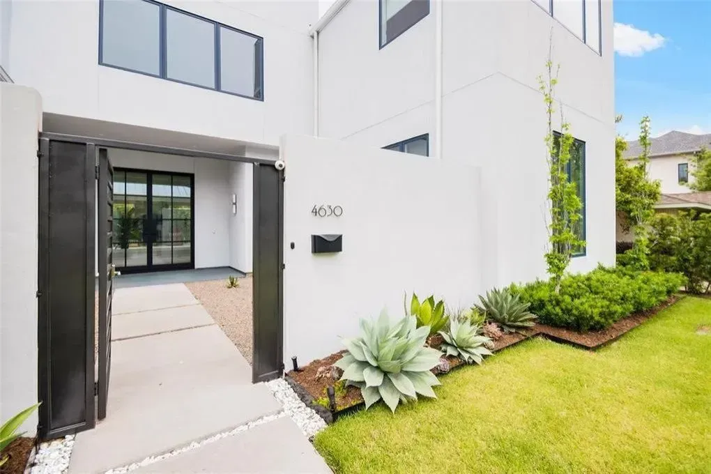 White modern home exterior with open black gate, front yard with landscaping.