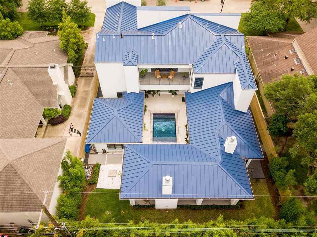 Aerial view of a white house with a blue metal roof, a central pool, and lush green landscaping.