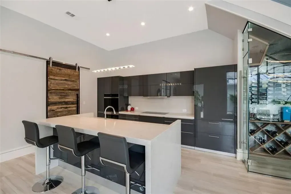 Modern kitchen with gray cabinetry, white countertops, island with bar stools, and a wine cellar.