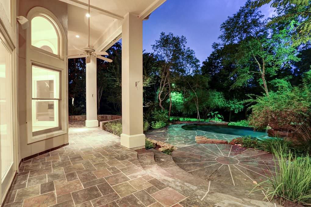 Covered patio with stone floor and view of pool and trees at dusk.