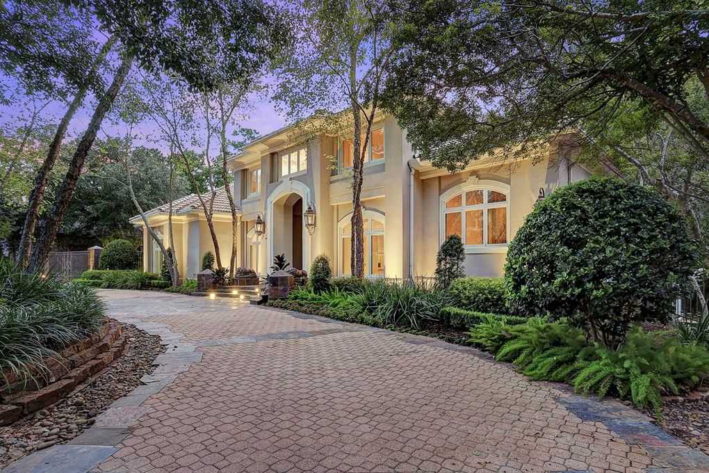Elegant house with a long, patterned driveway surrounded by lush greenery, at dusk.