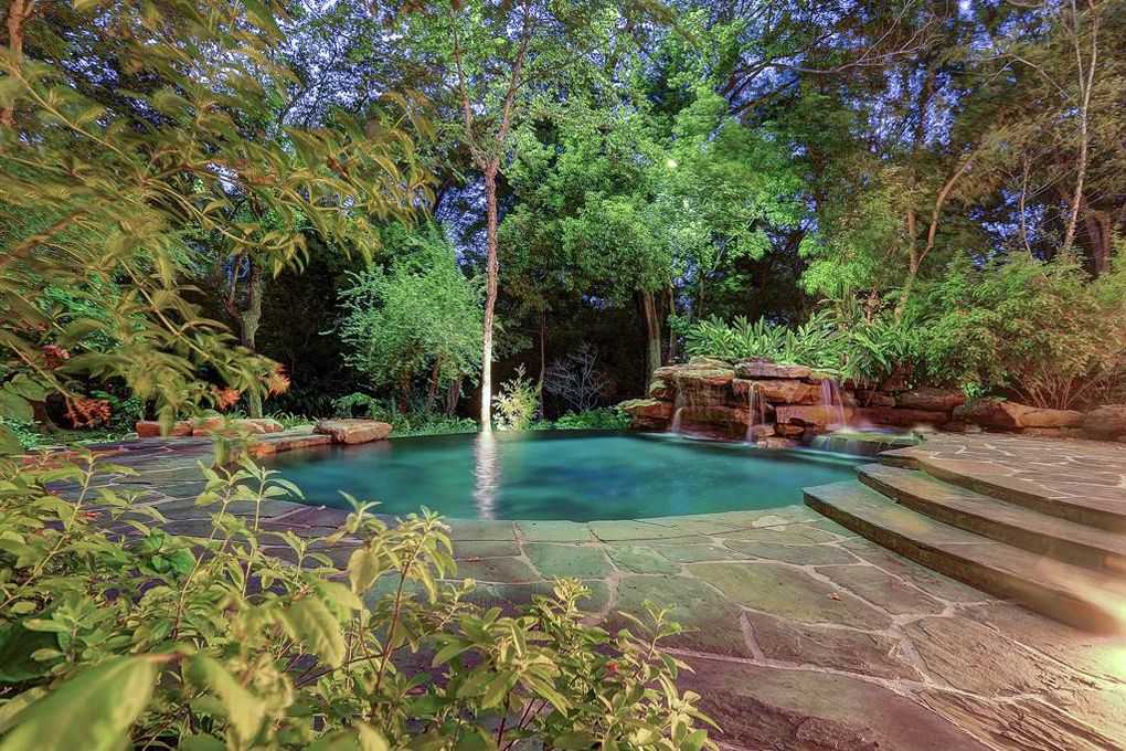 A natural, turquoise-colored pool surrounded by greenery and stone steps, lit by warm lights.