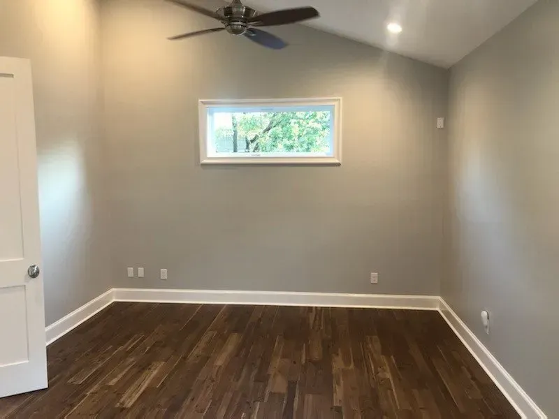 Empty bedroom with gray walls, wood floor, white trim, and a small window.