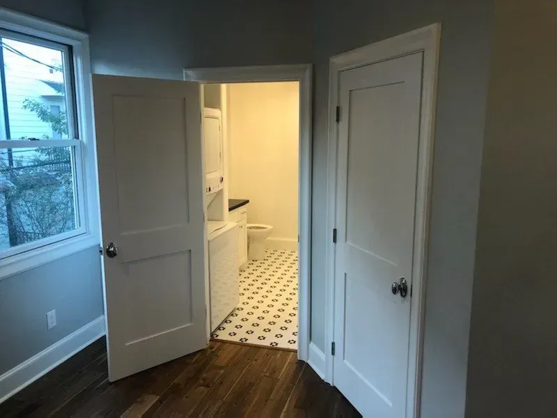 Two white doors opening into a laundry room with a washer, dryer, and patterned floor.