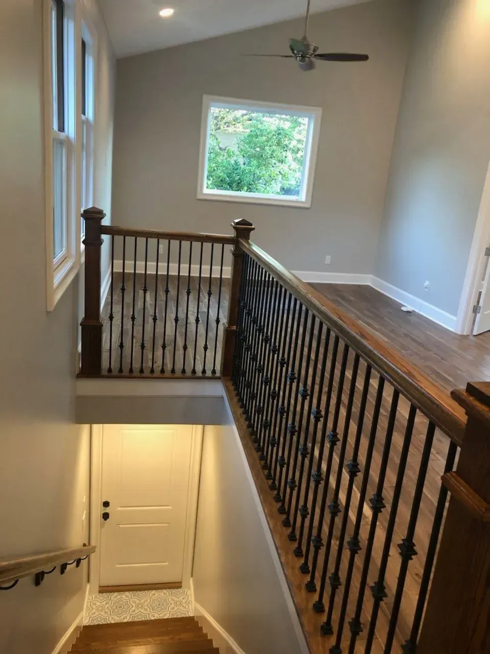 Interior view of a landing with stairs, dark wood railing, and an upper window with natural light.