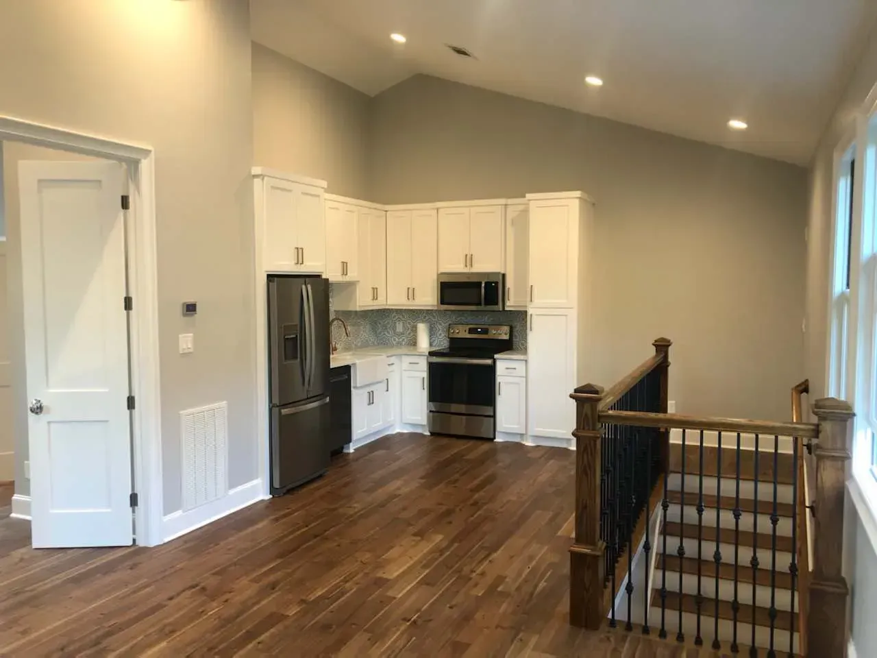 Kitchen with white cabinets, stainless steel appliances, and wood floors. Staircase on the right.