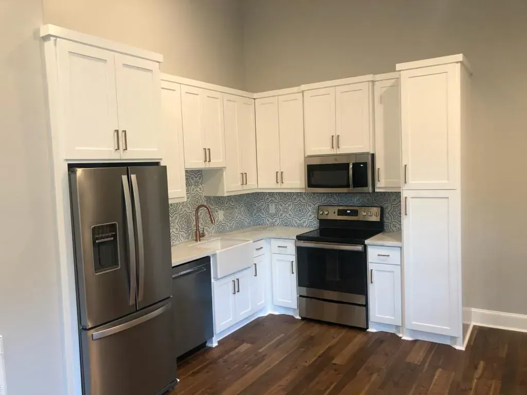 White kitchen with stainless steel appliances, white cabinets, and wood flooring.