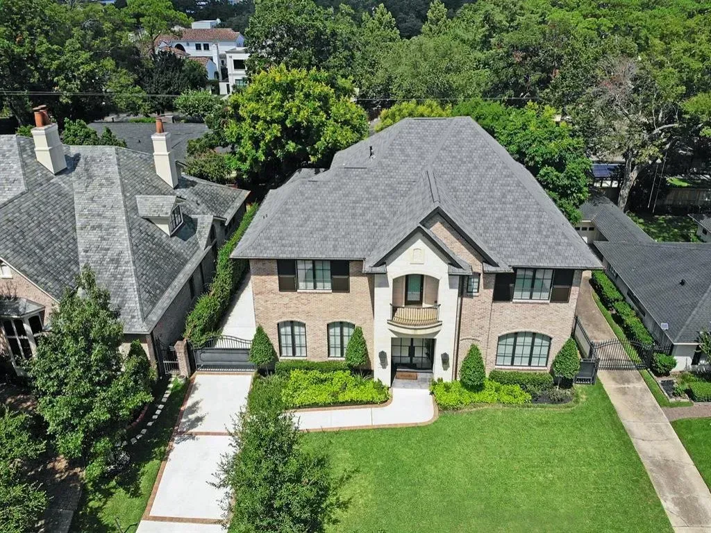 Two-story brick house with a gray roof and manicured lawn. The house is surrounded by trees.