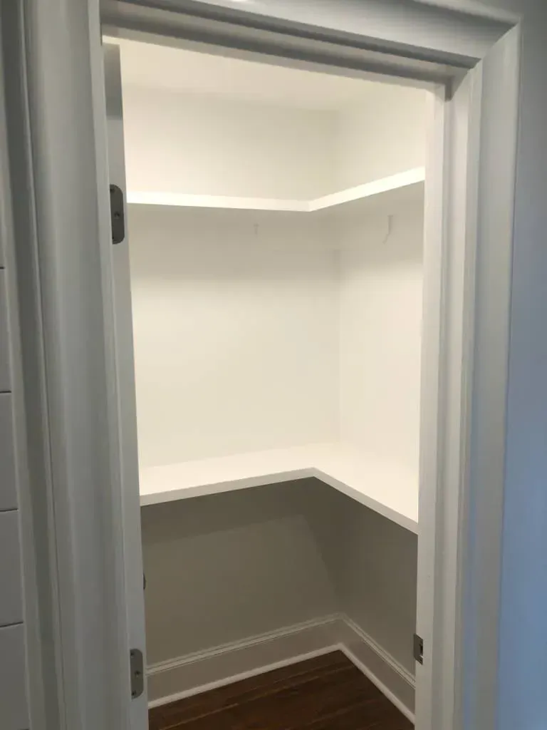 White pantry with shelves, wooden floor, open door frame.