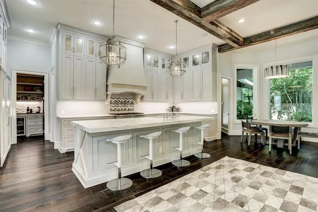Luxurious white kitchen with island, seating, dark wood floors, and a dining area.