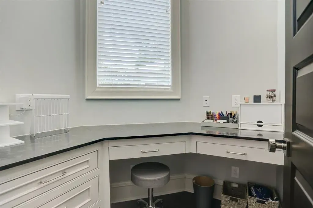 L-shaped desk in a room with a window. The desk has drawers and a stool, with storage baskets nearby.
