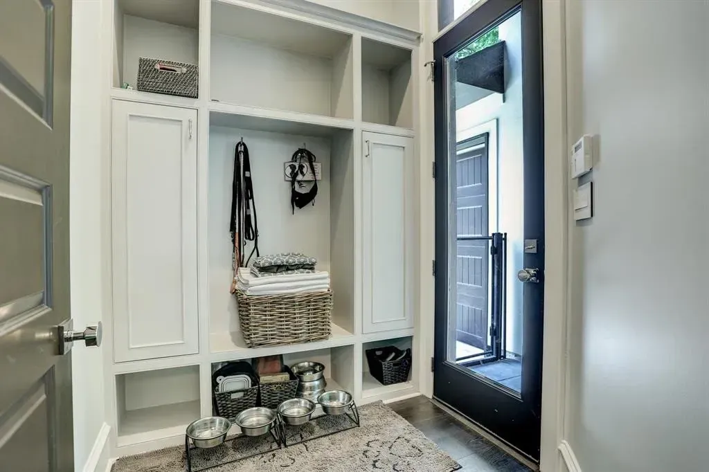 White built-in storage unit with shelves and cabinets near an exterior door; dog bowls in foreground.