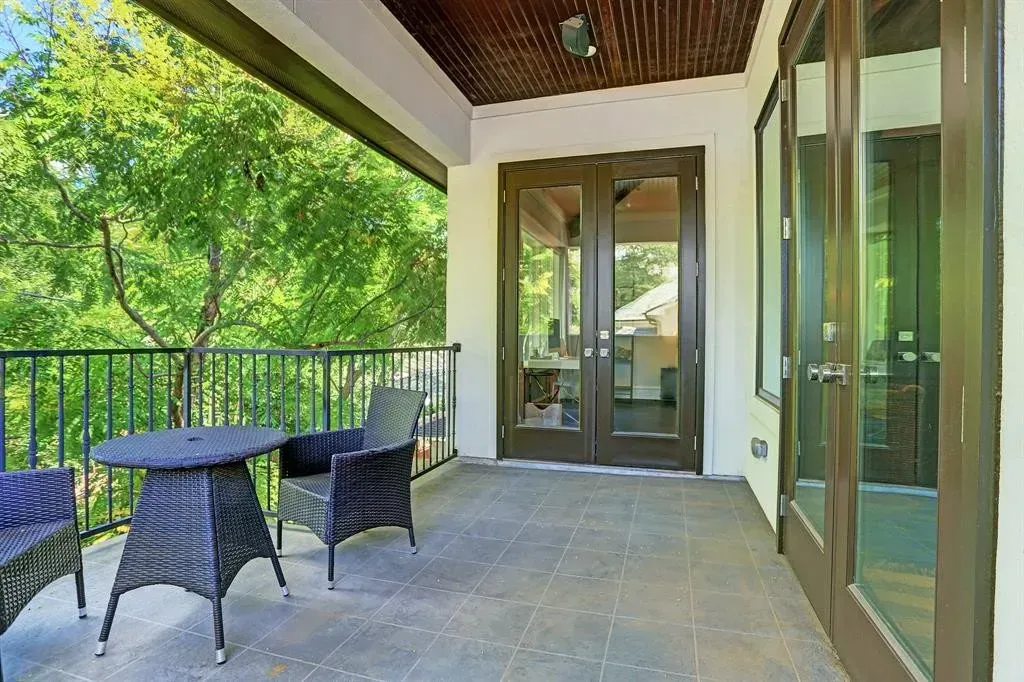 Balcony with a table and chairs, overlooking trees. French doors and glass windows visible.