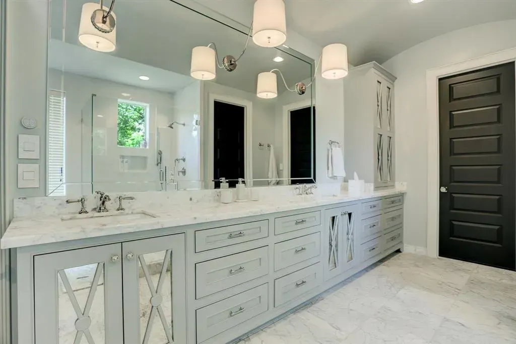 Bright modern bathroom with large mirror, gray cabinets, white marble countertop, and black doors.