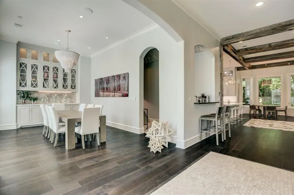 Spacious dining room with wooden floors, white chairs, chandelier, and a view into another room.