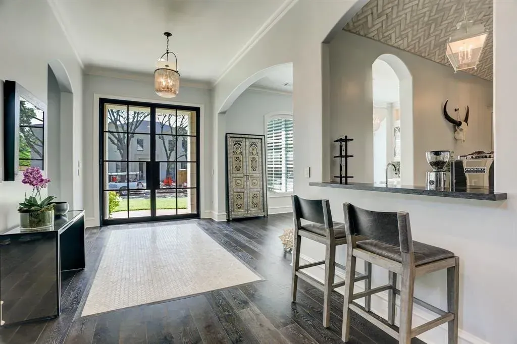 Spacious home entryway with black framed double doors, rug, wooden floors, arched doorway, and bar seating.