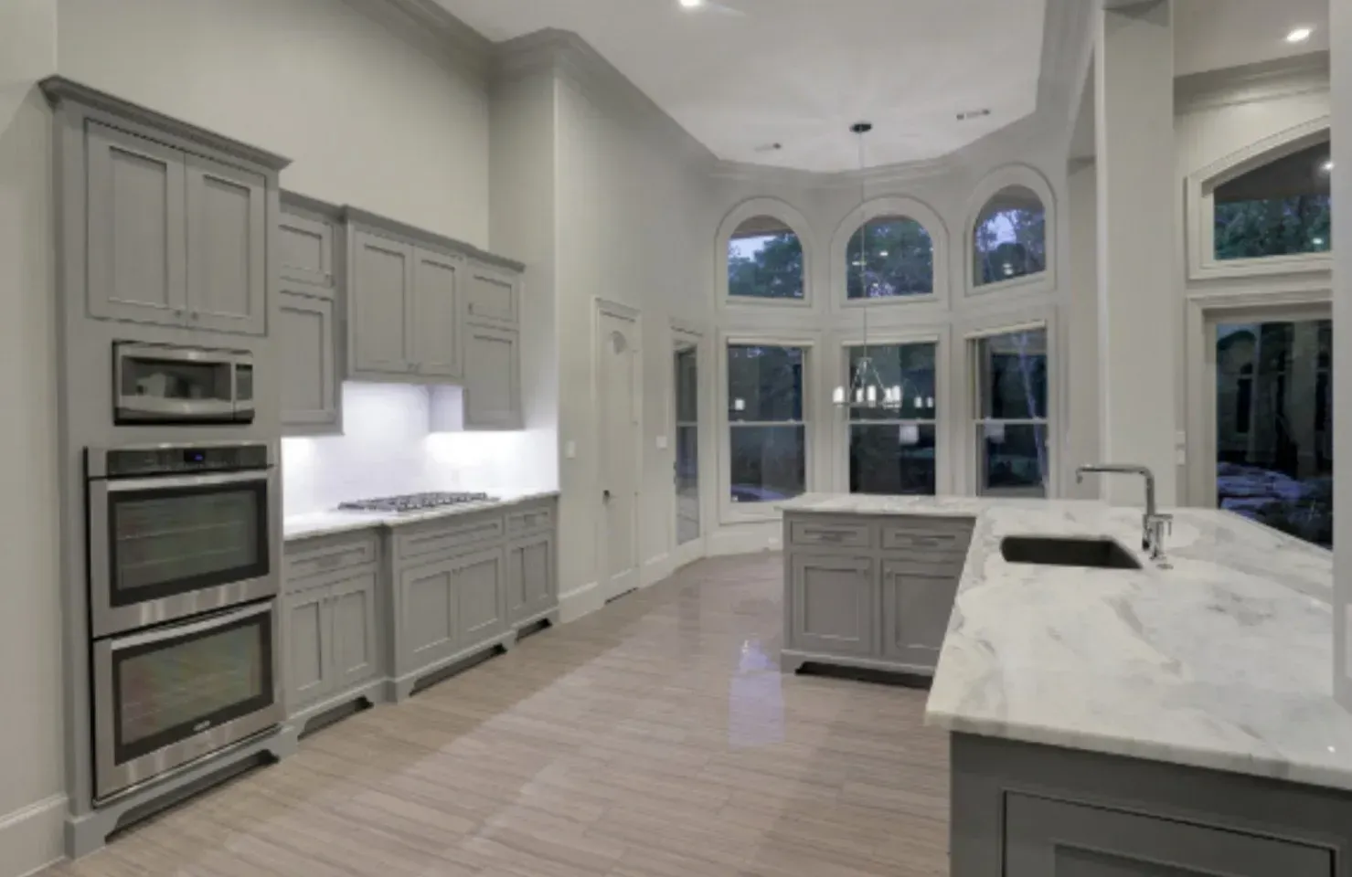 Gray kitchen with marble countertops, cabinets, appliances, and arched windows.
