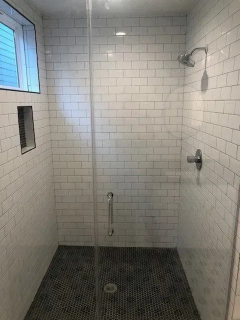 Shower stall with white subway tile walls, dark hexagon tile floor, and glass door.