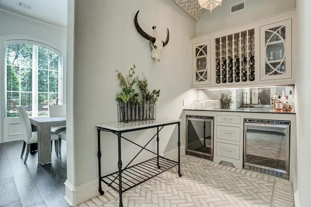 Butler's pantry with wine storage, a bar cart, and an arched window. Light-colored walls and a herringbone tile floor.