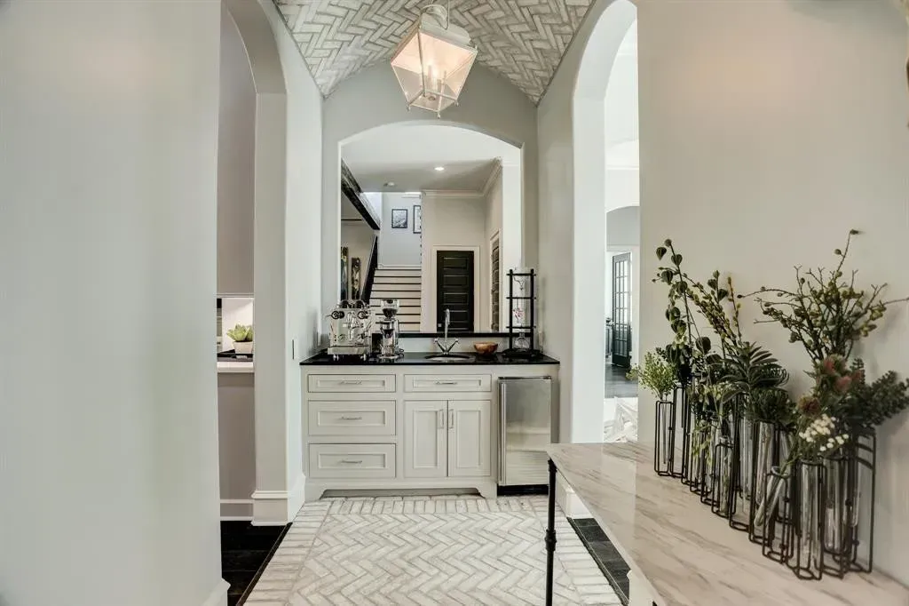 Hallway with white walls, arched doorways, a small bar area with a white cabinet, and a patterned ceiling.