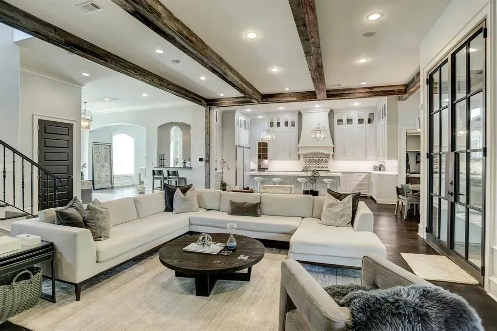 Spacious living room with white sectional, wooden beams, and a view of the kitchen and dining area.