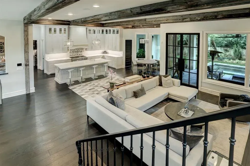 Spacious, modern living space with a white kitchen, sectional sofa, and exposed wooden beams.