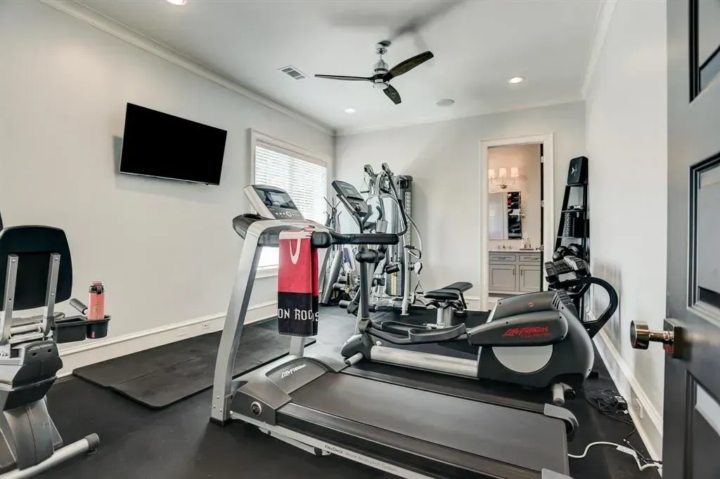 Home gym with exercise equipment: treadmill, elliptical, weights, and a TV. Light gray walls.