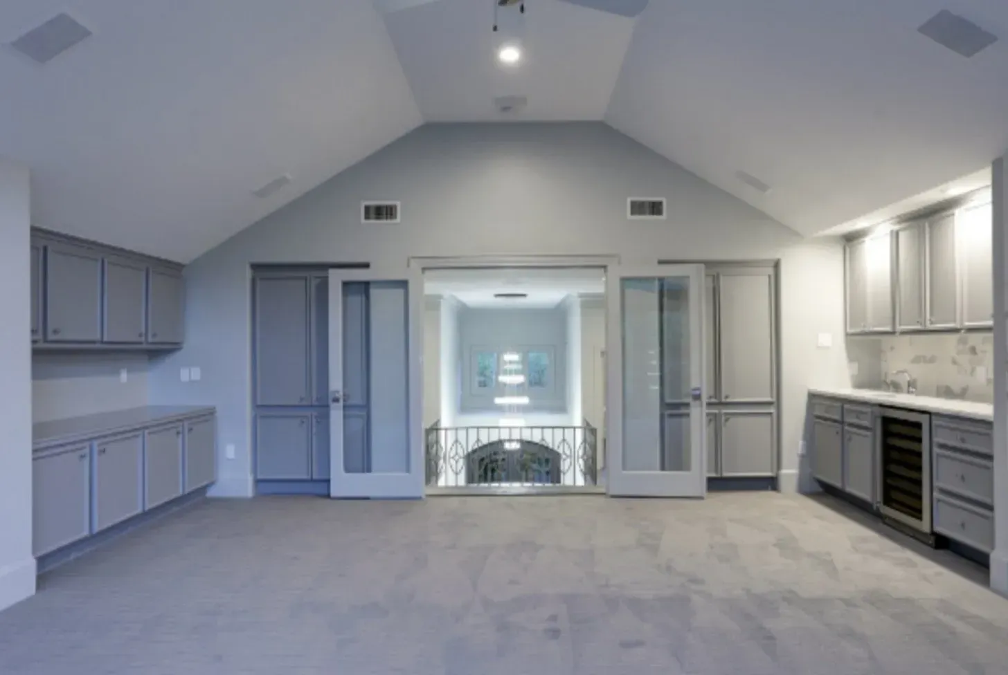 Empty, gray-toned room with vaulted ceiling, cabinets, doors, and a staircase leading down.