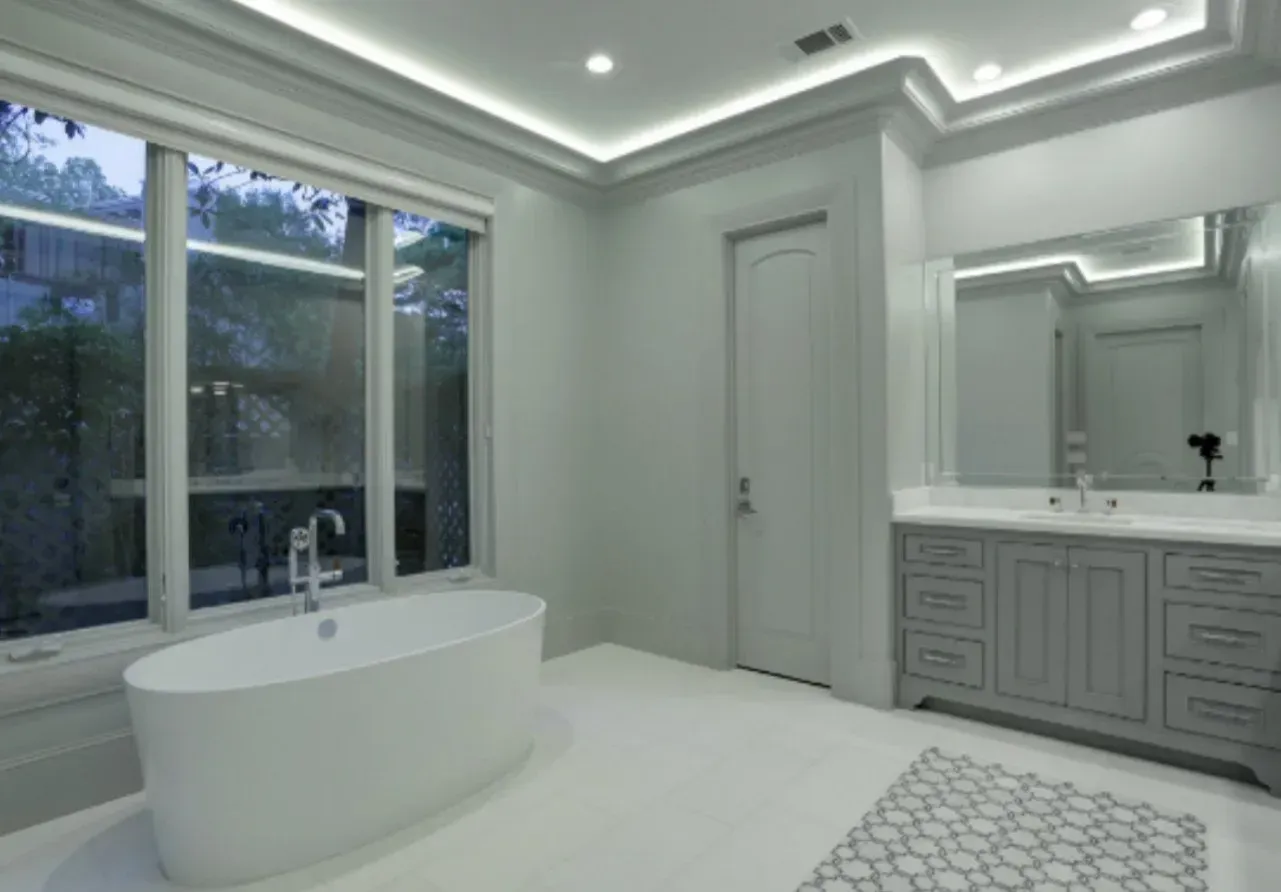 White bathroom with a freestanding tub near a large window, gray vanity, and decorative ceiling lights.