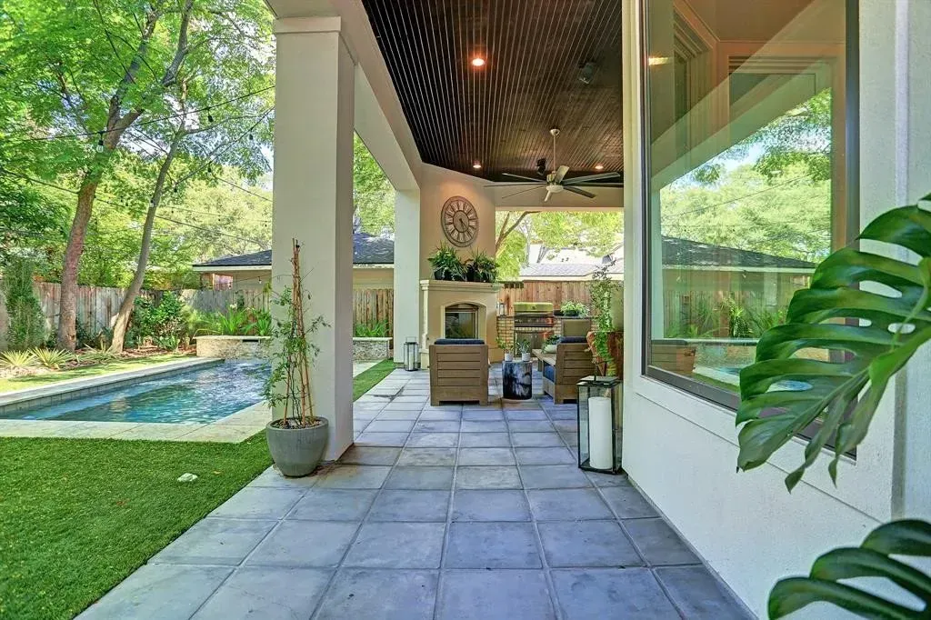 Patio overlooking pool and yard, with seating, fireplace, and plants; stone tile floor, green grass.