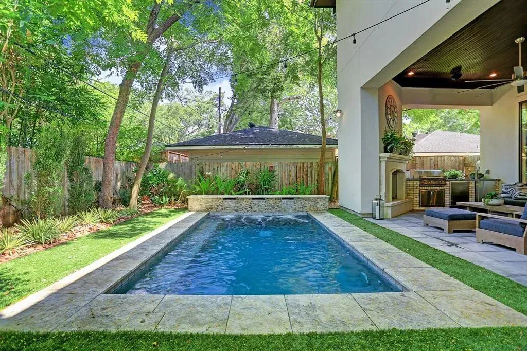 Backyard pool with stone surround, lush greenery, and covered patio.
