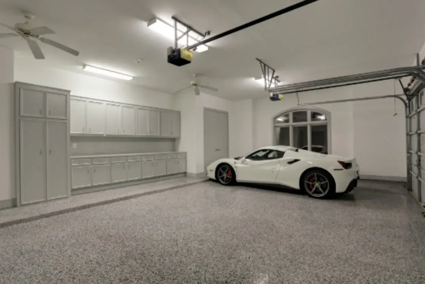 White sports car in a modern, well-lit garage with gray cabinets and speckled flooring.