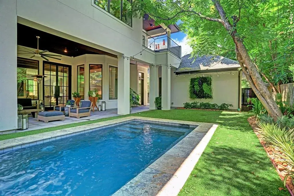 Pool and yard of a modern house, with patio furniture and lush greenery.
