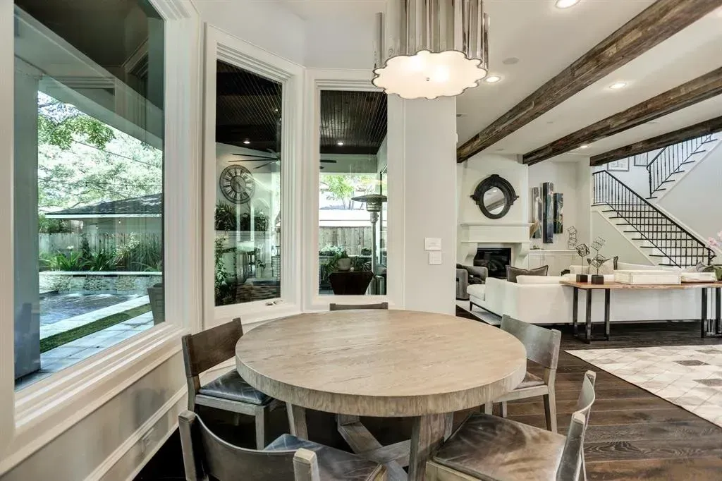 Dining area with round table, chairs, and large windows.  Beams and staircase visible in background.