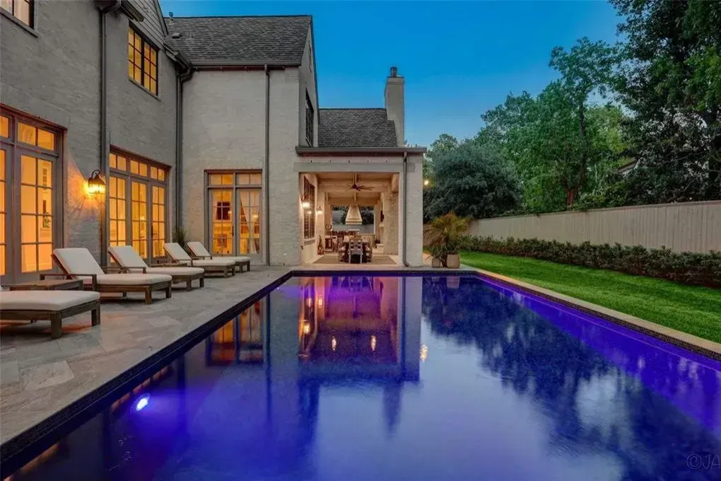 A luxury home with a rectangular pool, lounge chairs, and an outdoor dining area at dusk.