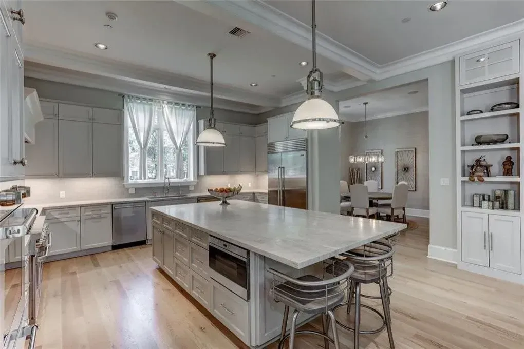 Modern kitchen with gray cabinets, marble island, stainless steel appliances, and wood floor.