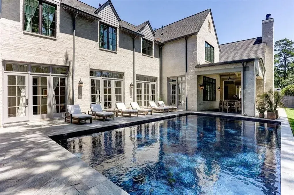Backyard with pool, lounge chairs, and two-story brick home on sunny day.