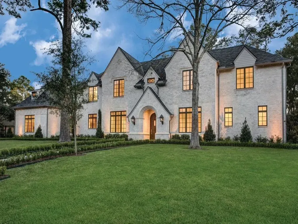 Large, light brick house with dark windows, a manicured lawn, and trees.