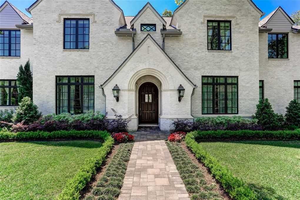 A cream-colored two-story house with a brick walkway, green lawn, and dark-framed windows.