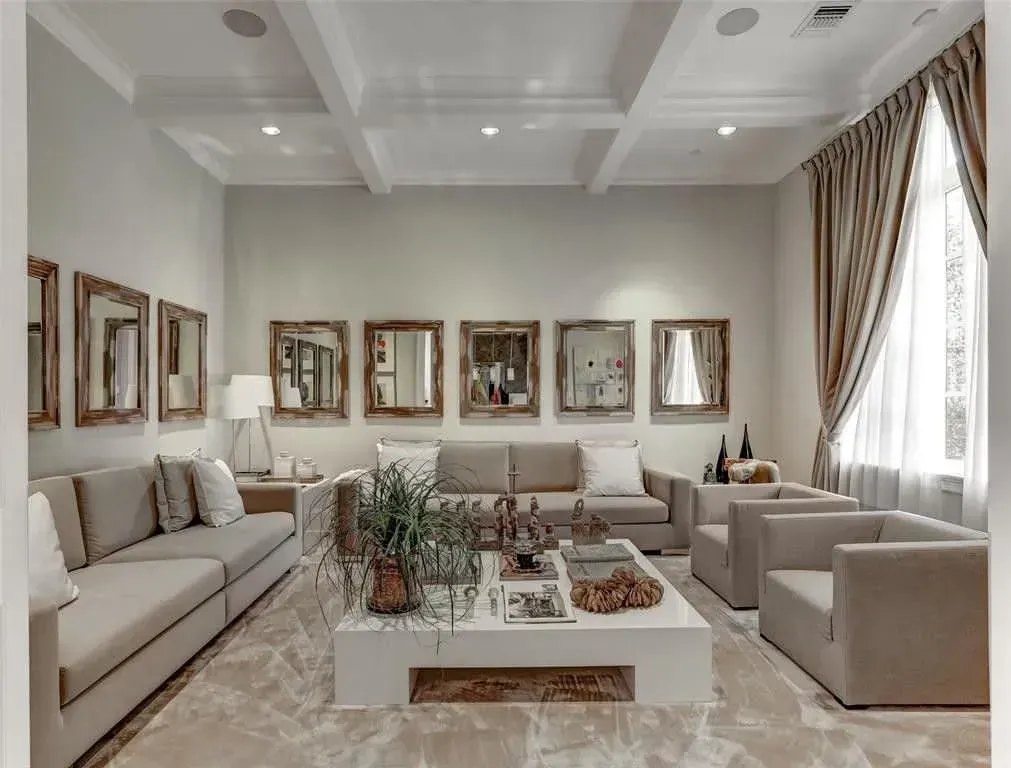 Living room with beige furniture, mirrors, and a large white coffee table.