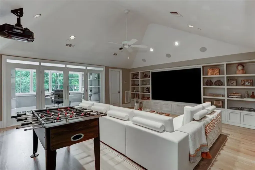 Game room with foosball, white sectional, large TV, and built-in shelving.