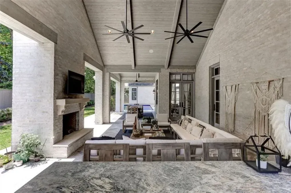 Covered outdoor patio with fireplace, seating, ceiling fans, and neutral color scheme.