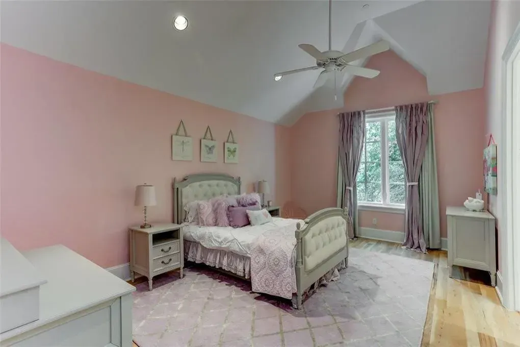 Pink bedroom with bed, nightstands, and window with purple curtains.