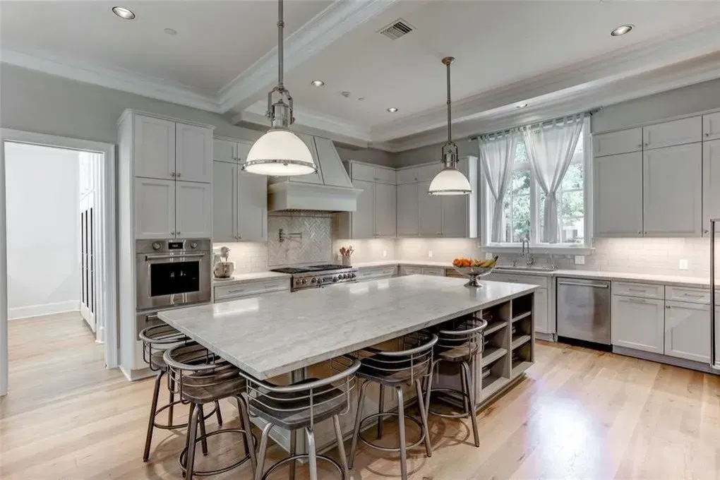 Spacious, modern kitchen with light gray cabinets, large island, stainless steel appliances, and wood flooring.