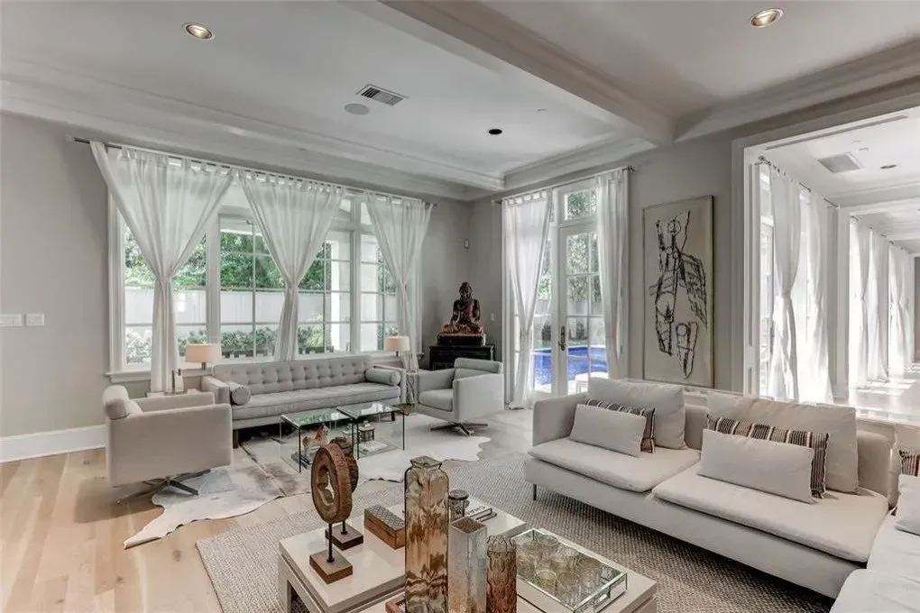 Spacious living room with light-colored furniture, large windows, and an outdoor view.