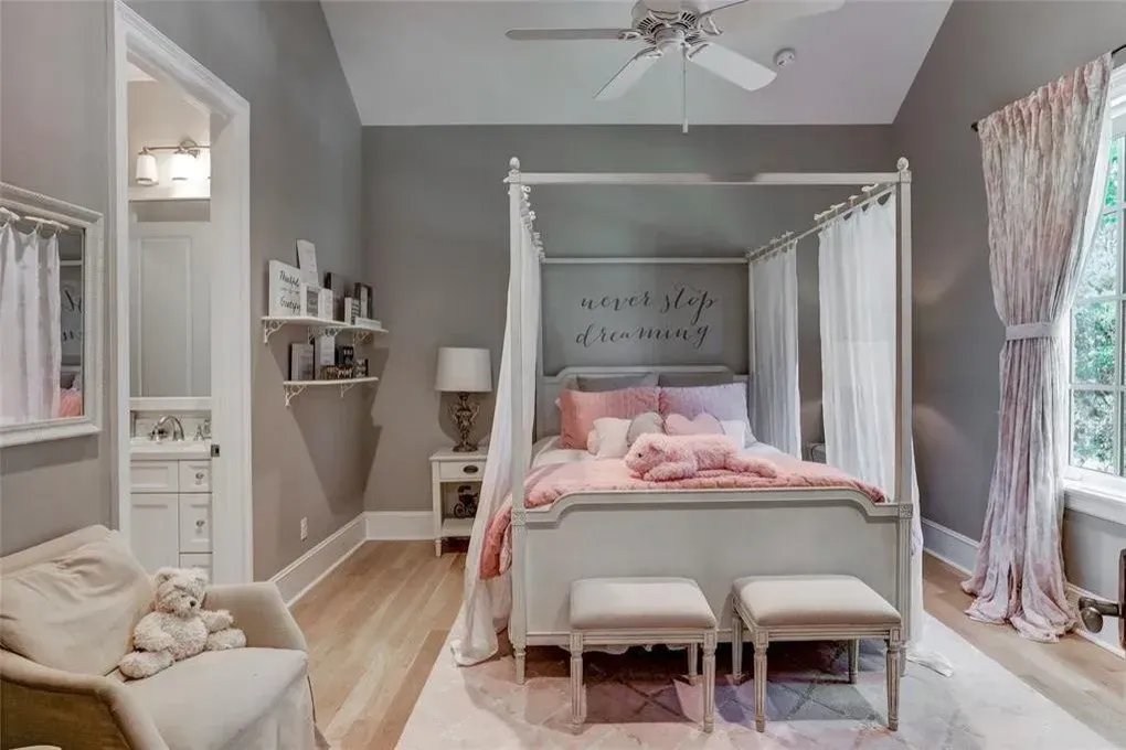 Gray bedroom with canopy bed, pink and white bedding, and a small chair.