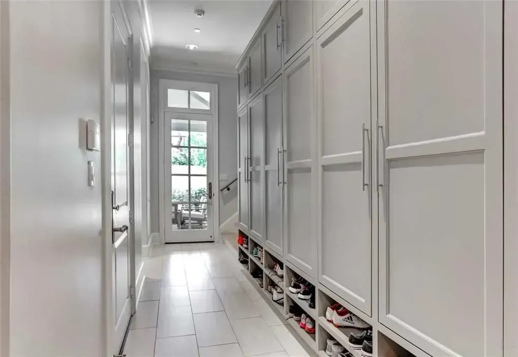 Long hallway with built-in white cabinets, shoe storage, and door with glass panels.