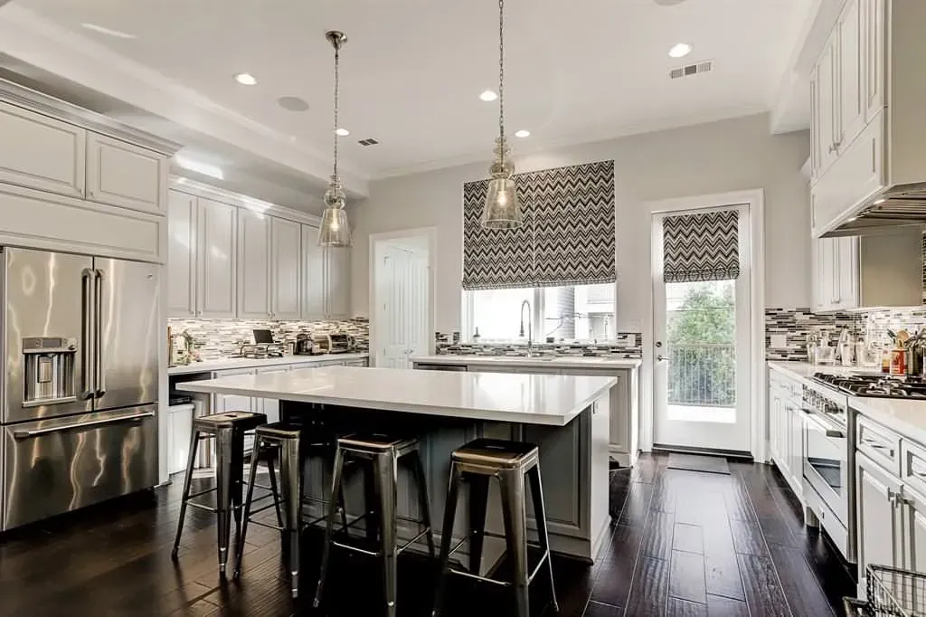 Spacious, light-filled kitchen with a large island, stainless steel appliances, dark wood floors, and hanging pendant lights.