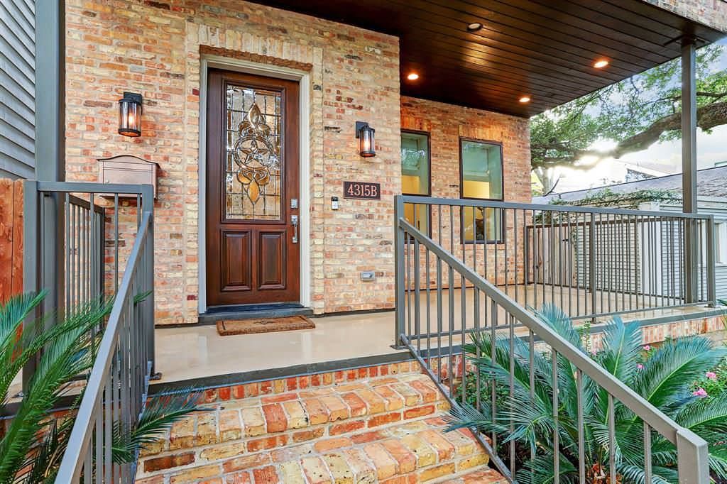 Brick house exterior with a porch, brown door, and metal railings.