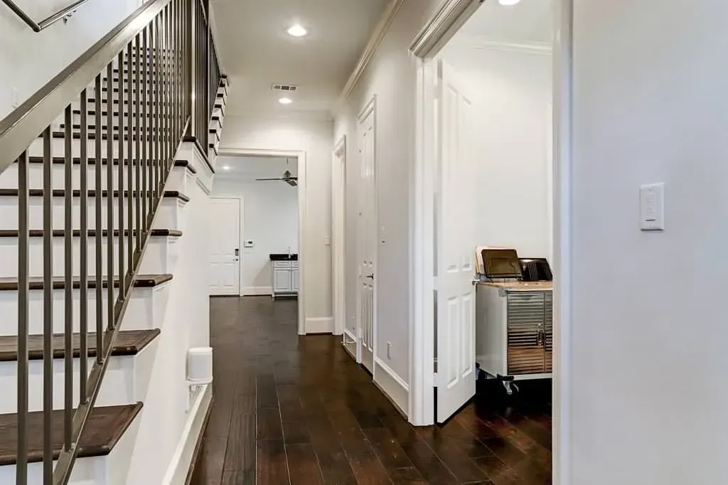 Hallway with dark wood floor, white walls, and stairs with metal railing.